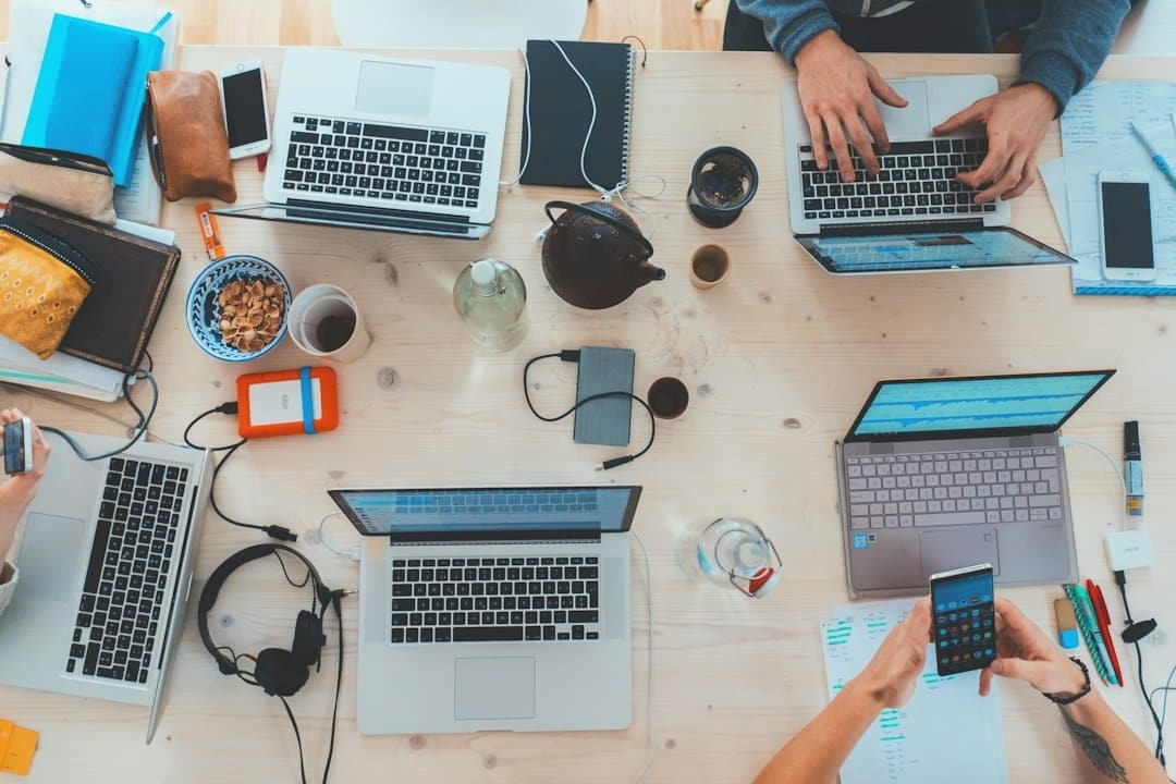 Hands using laptops and smartphones on a wooden table.